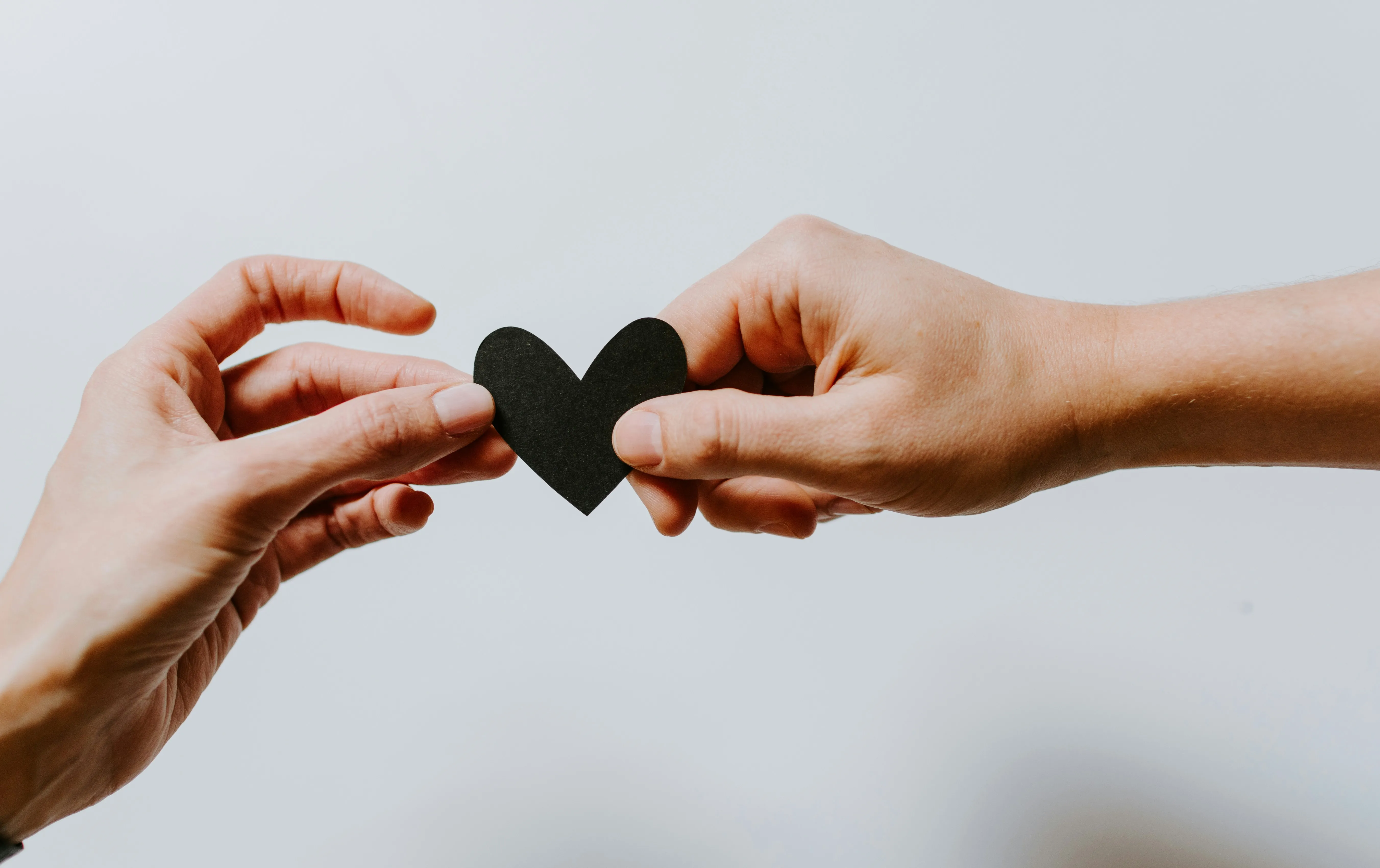 Two hands passing a small paper heart between them